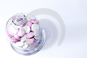 Pink and white chocolate peppermint candies in a glass jar on a white background