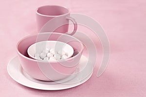 Pink and white crockery with sugar dragees inside on a pink cloth background