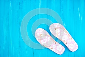 Pink with white flowers flip flop sandals beach shoes on blue wooden floor. Top view and copy space.