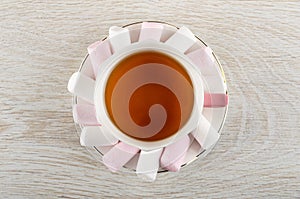 Pink and white marshmallow, cup of tea on saucer on table. Top view