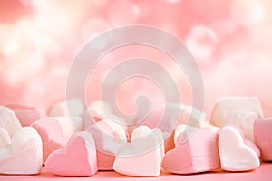 Pink and white marshmallows in the shape of hearts on a pink abstract background with bokeh.