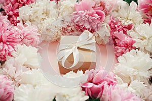 Pink and white peonies with gift box on pastel pink paper. Copy space. Happy mothers day, floral greeting card mockup.