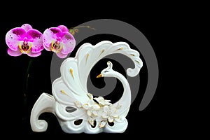 Pink and white phalaenopsis orchids and a swan shape decorative flower vase against dark background