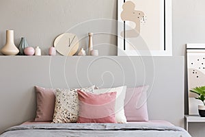 Pink and white pillows on grey bed in pastel bedroom interior with poster on bedhead. Real photo