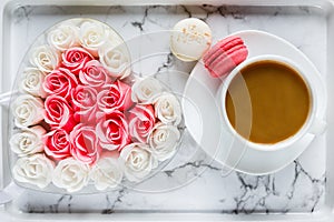 Pink and white roses in heart shaped box and coffee cup on marble table background. Delicious sweets and coffee break. Gift