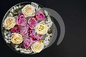 Pink and white roses and limonium in a bowl with water on a black background