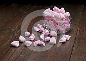 Pink and white striped candy in small glass bowl on brown wooden surface