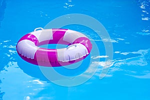 Pink-white swimming pool ring, float in refreshing blue water. Sunny day at resort.