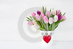 Pink and white tulips bouquet in white vase decorated with red heart. Valentines Day concept.