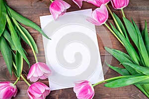 Pink white tulips and white sheet of paper on dark brown wooden background, horizontal, copy space, top view