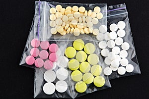 Pink, white and yellow pills in plastic bags on black background