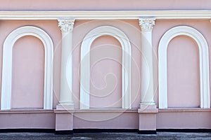 Pink windowless facade of the building with white columns and arches. Beautiful exterior. Background, wallpaper.