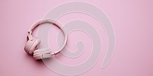 Pink wireless headphones on a pink background, banner. Top view on modern gadget