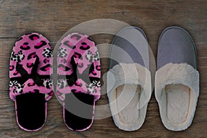 Pink women`s home slippers with black bow and gray men`s sneakers stand on the floor, concept of comfortable shoes for rest, rel