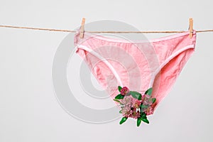 Pink women`s underwear decorated with flowers on clothesline isolated on white, concept photography for feminist blog