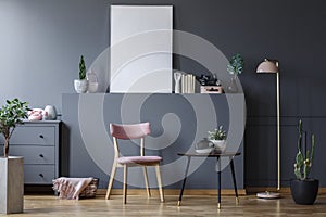 Pink wooden chair at black table in grey living room interior with mockup of empty poster