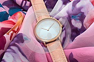 Pink wrist watch on colourful silk fabric background