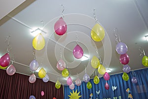 Pink and yellow balloons float on the white ceiling in the room for the party. Wedding or children birthday party