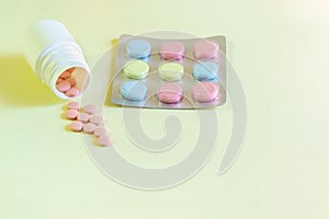 Pink, yellow and blue tablets on a yellow table. Multicolored medicines for the prevention and treatment