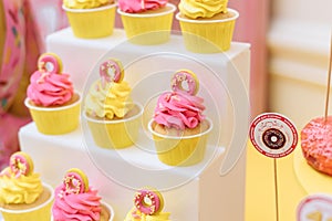 Pink and yellow cupcakes with mastic doughnuts. Bright and cheerful sweets for the holiday
