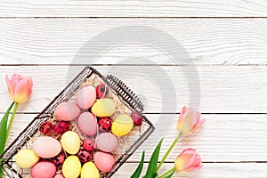 Pink and yellow easter eggs in basket with tulip flowers on white wooden background. Spring concept. Top view, copy space