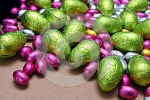Pink, yellow, green and silver foil wrapped chocolate easter eggs with larger lime green eggs, on a pale wood background.