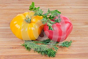 Pink and yellow tomatoes, greens on a wooden surface