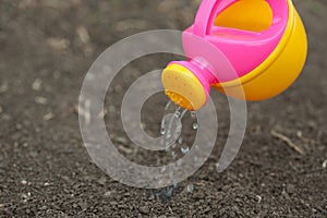 A pink yellow watering can water the ground. Drops of water spill, dissipate moisturize the earth. Help fight the drought.