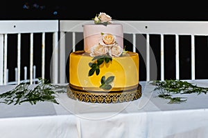 Pink and yellow wedding cake standing on table with colorful decorations around