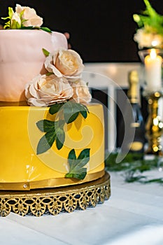 Pink and yellow wedding cake standing on table with colorful decorations around