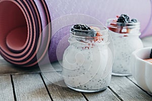 Pink yoga mat and Pudding with chia seeds, yogurt and fresh fruits: Strawberries, blueberries and blackberries in glass jars on w