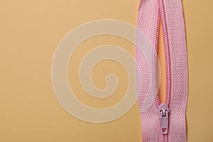 Pink zipper on beige background, close up