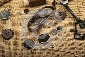Pins of various sizes, tailor`s scissors, and various buttons on coarse-textured burlap. Close up