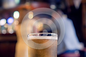 Pint glass of cold lager beer of cider in focus. Well dressed woman and man out of focus in the background. Date of flirt concept