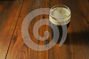 Pint glass of a dark stout beer on a wooden table in a pub. Alcohol beverage industry concept. Copy space
