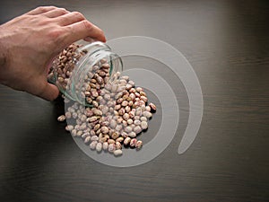 Pinto bean seeds hand dish.Pinto bean seeds are poured from a glass jar on brown wooden surface