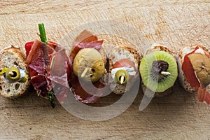 Pintxo Set: Olive, Anchovy, Cherry tomato, kiwi, Raisin, Cured Ham, Mushroom, bread in a rustic board