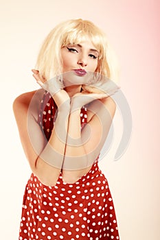 Pinup girl in blond wig retro dress blowing a kiss