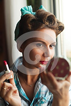 Pinup look dressed woman paints her lips with red lipstick