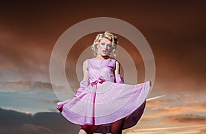 Pinup style woman in summer dress on dramatic sky. Beautiful girl in stylish fashion clothes in summer. Fashion woman