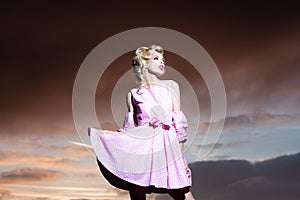 Pinup style woman in summer dress on dramatic sky. Fashion outdoor photo of gorgeous sensual woman in elegant dress