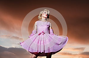 Pinup style woman in summer dress on dramatic sky. Fashionable young model in style dress. Fashion woman in summer.