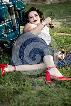 A pinup woman in a vintage dress posed next to the old motorcycle