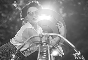 A pinup woman in a vintage dress posed next to the old motorcycle