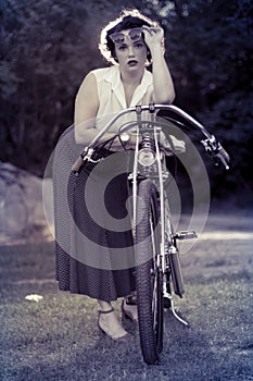 A pinup woman in a vintage dress posed next to the old motorcycle