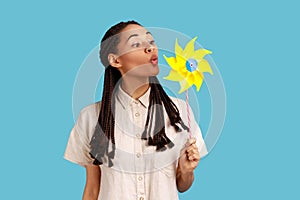 Woman blowing at paper windmill, playing with hand mill on stick, having fun.