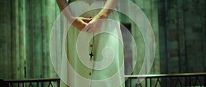 Pious senior woman praying in the old church. Parishioner holding a religious cross in hand and walks along the pews.