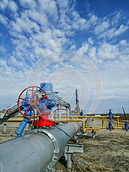 Pipe fittings of gas wells against the background of a drilling rig.