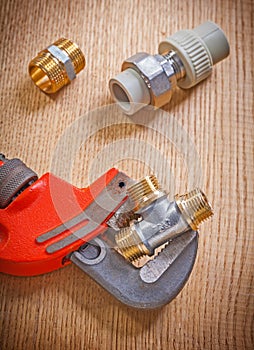 Pipe fixtures and monkey wrench on wooden board close up