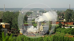 Pipes of industrial plant smoke among green trees and nature in Alapaevsk.